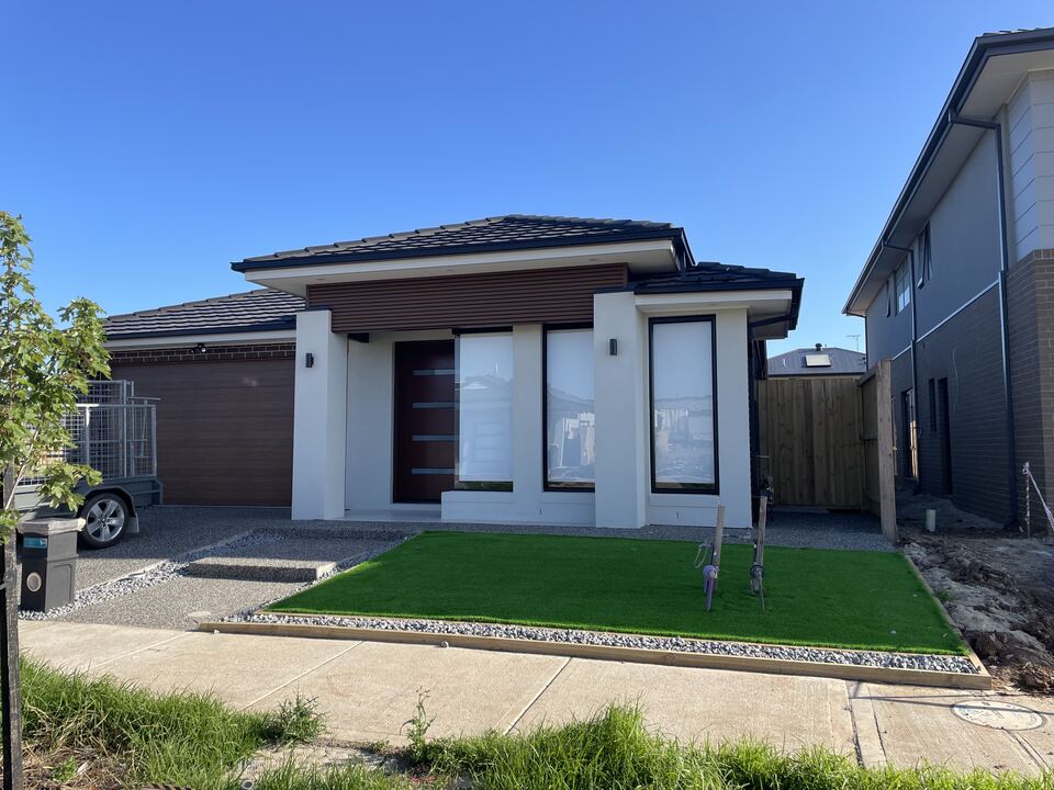 Front of our Lucania Crescent home: a single-storey home with white rendered pillars, tall black-framed windows, a dark timber-look feature over the entry and a timber-look garage door